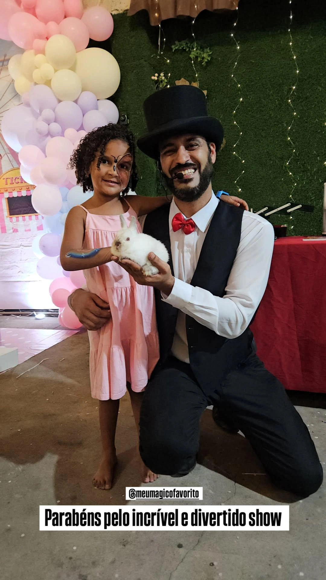 Mágico agachado ao lado de uma criança fantasiada, segurando um coelho branco em uma festa de aniversário