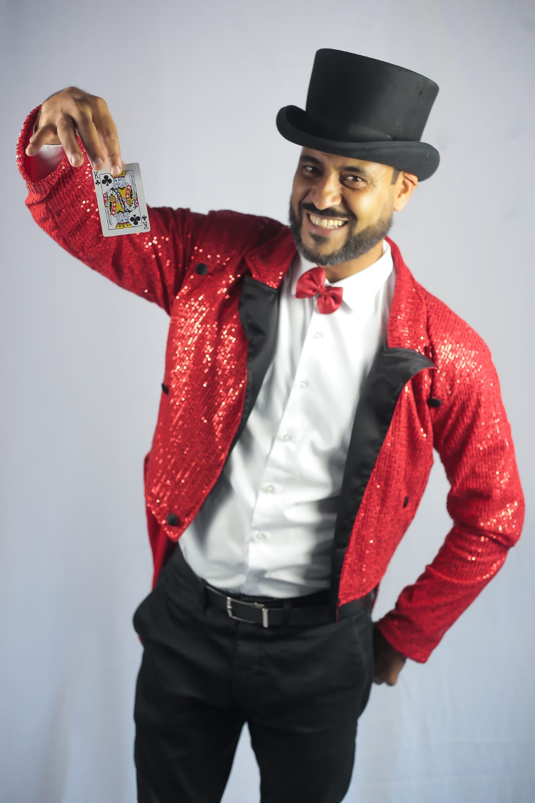 Mágico de paletó vermelho de paetês e cartola, sorrindo ao exibir uma carta de baralho